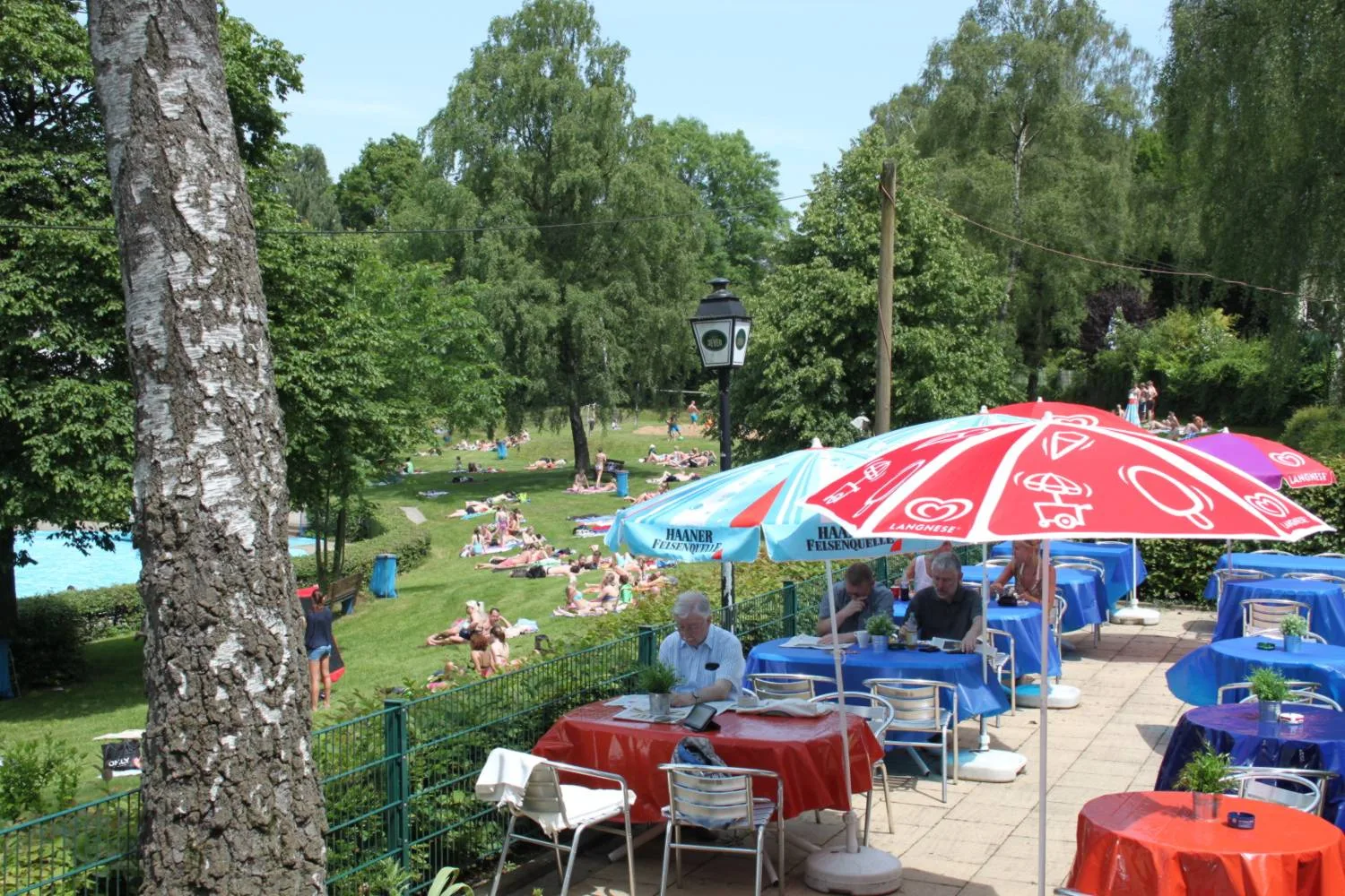 Sonnenterrasse mit Tischen und Schirmen über der Liegewiese